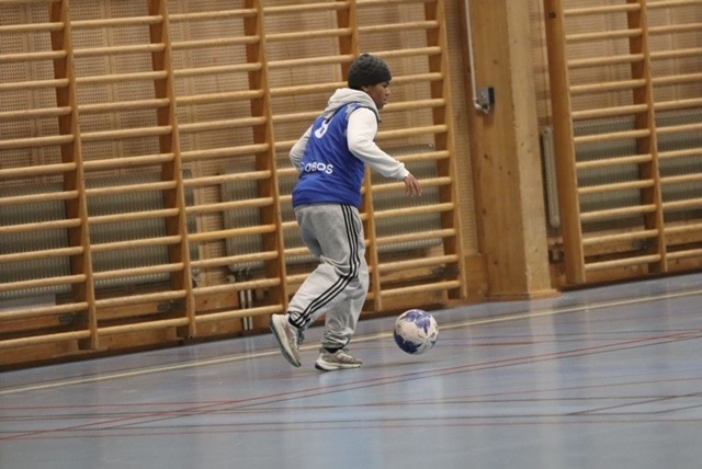 Spelare som dribblar en fotboll i en inomhushall.