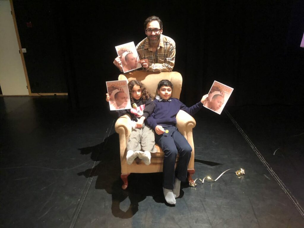 En pappa och hans två barn, en flicka och en pojke, som sitter i en fåtölj.